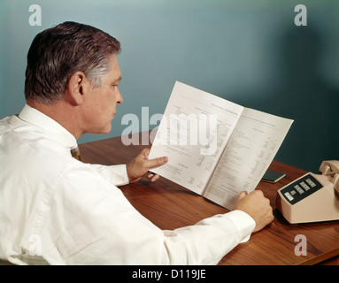 1960S 1970S BUSINESS-MANN AM SCHREIBTISCH LESEN EINES DOKUMENTS FINANZBERICHT Stockfoto