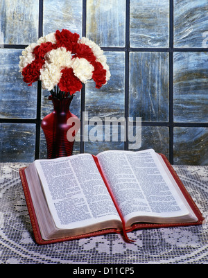 ROTEN UND WEIßEN NELKEN IN ROTE VASE MIT BIBEL AUF TABELLE ÖFFNEN, UM DAS BUCH DER PREDIGER Stockfoto