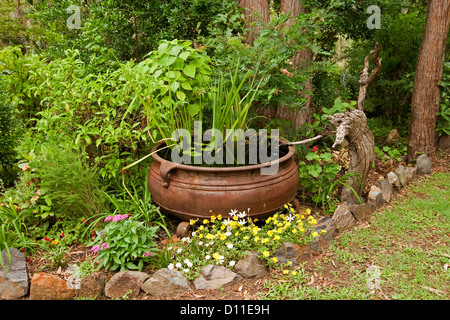 Reich verzierte Gartenteich - großen rostigen Kessel als ein Wasserspiel mit Wasserpflanzen Pflanzen und umgeben von bunt blühenden Pflanzen Stockfoto