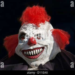 Porträt des Gesichts der Monster / clown - Mann trägt eine weiße Maske mit riesigen Zähnen, rote Nase und rote Haare vor schwarzem Hintergrund Stockfoto