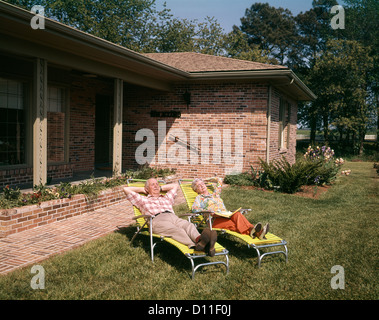 1960ER JAHRE ÄLTERES PAAR GARTENSTÜHLEN ENTSPANNEN IN HOF EIN ZIEGELHAUS Stockfoto