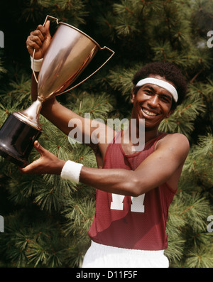 1970ER JAHRE AFRIKANISCH-AMERIKANISCHER MANN TRACK AND FIELD SIEGER TROPHÄE HOCHHALTEN Stockfoto