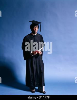 1970ER JAHREN AFROAMERIKANISCHE MANN GRADUATE TRAGEN SCHWARZE KAPPE KLEID DIPLOM BLICK IN DIE KAMERA HALTEN Stockfoto
