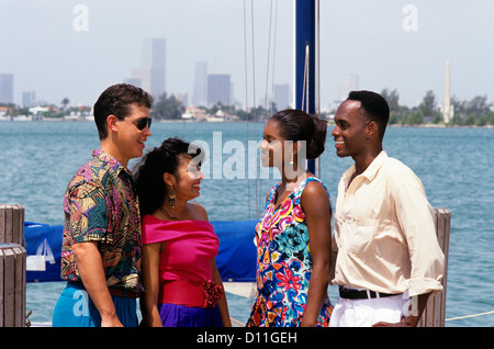 DER 1990ER JAHRE ZWEI PAARE KAUKASISCHEN & AFROAMERIKANISCHEN AM DOCK VON SEGELBOOT SKYLINE VON MIAMI Stockfoto