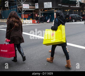 Shopper mit Tory Burch und American Girl Einkaufstüten an der Madison Avenue in New York Stockfoto