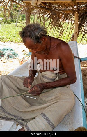 Sri Lanka Fischer Reparatur sein Fischernetz sitzend auf seinem kleinen Boot, Waikkal, Sri Lanka Stockfoto