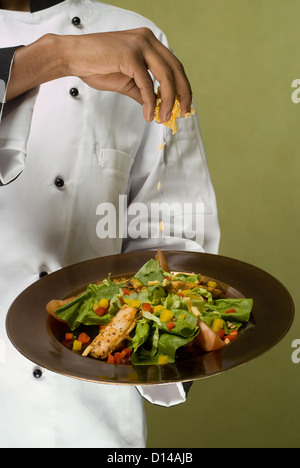 Nahaufnahme von Küchenchef Prise Käse auf Teller mit gesunde Hähnchensalat Stockfoto