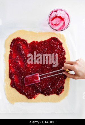 Hand, die Marmelade auf dem Teig verteilen Stockfoto