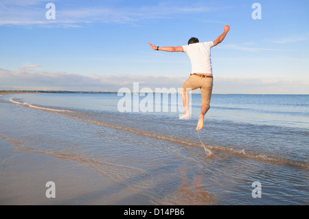 Mann springt vor Freude in Wellen am Strand Stockfoto