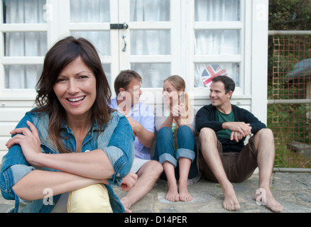 Frau sitzt mit Familie vor Haus Stockfoto