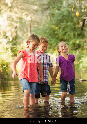 USA, Utah, Lehi, drei Kinder (4-5, 6 und 7) Hand in Hand und gehen gemeinsam in kleinen Bach Stockfoto