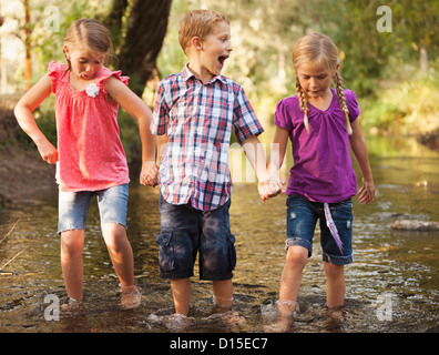 USA, Utah, Lehi, drei Kinder (4-5, 6 und 7) Hand in Hand und gehen gemeinsam in kleinen Bach Stockfoto