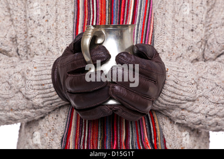 Nahaufnahme eines Mannes in wollene Pullover, Schal und Handschuhe halten einen Zinn Becher Glühwein. Schwerpunkt liegt auf den Händen und Krug. Stockfoto