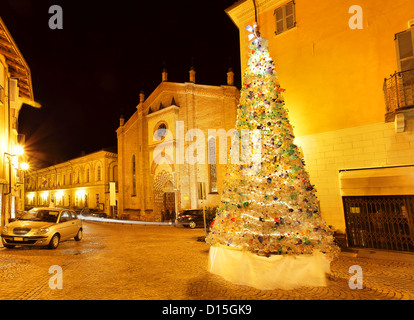 Beleuchteter Weihnachtsbaum aus Plastikflaschen am kleinen Platz vor der alten Kirche am Abend in Alba, Italien hergestellt. Stockfoto