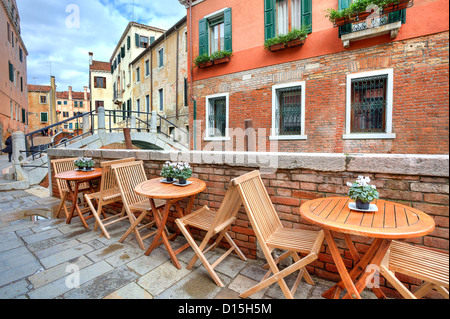 Holztischen auf schmalen Straße zwischen den typischen bunten Häusern und kleinen Brücke in Venedig, Italien. Stockfoto