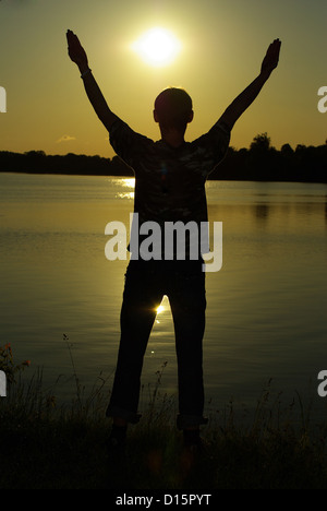 Ein Mann steht auf gegen eine Sonne mit gehievt, die Hände Stockfoto