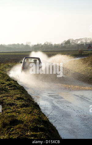 Ein Auto durchläuft Flut mit Geschwindigkeit kotzte Spray auf einer Straße in North Norfolk, Großbritannien. Die Straßen wurde wegen starkem Regen Herbst & das Regenwasser läuft aus der Felder auf den Highway überflutet. Stockfoto