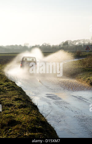 Ein Auto durchläuft Flut mit Geschwindigkeit kotzte Spray auf einer Straße in North Norfolk, Großbritannien. Die Straßen wurde wegen starkem Regen Herbst & das Regenwasser läuft aus der Felder auf den Highway überflutet. Stockfoto