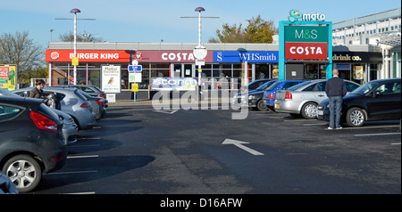 M1 Moto Autobahn-Tankstelle und Teil des belebten Parkplatzes mit Schildern für beliebte Geschäftsnamen am sonnigen Tag in Toddington in Bedfordshire England Großbritannien Stockfoto