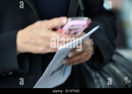 Nervöse Hände, die ein Smartphone handhaben, eine Hand hält ein Magazin und die andere. Eine Zweihandbedienung, zwei Daumen für SMS, Klicken. Stockfoto