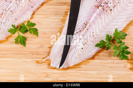 Tipp von Filetiermesser auf hautlos Weißfisch mit Gewürzen und Petersilie auf Bambus-Brett Stockfoto
