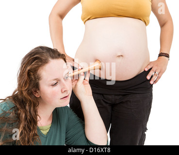 Hebamme am menschlichen Bauch hören. Schwangere Frau stehen, während Hebamme vorne sitzt. Stockfoto