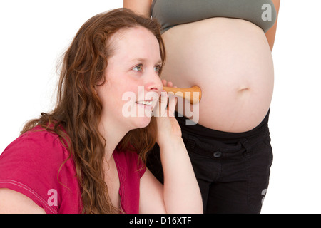 junge Hebamme am menschlichen Bauch hören. Schwangere Frau stehen, während Hebamme vorne sitzt. Stockfoto