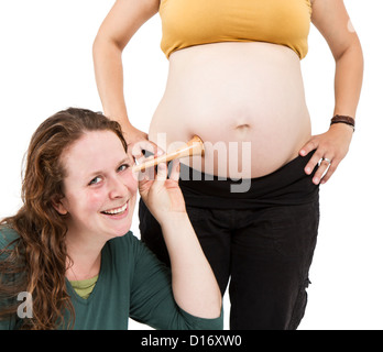 junge Hebamme am menschlichen Bauch hören. Schwangere Frau stehen, während Hebamme vorne sitzt. Stockfoto