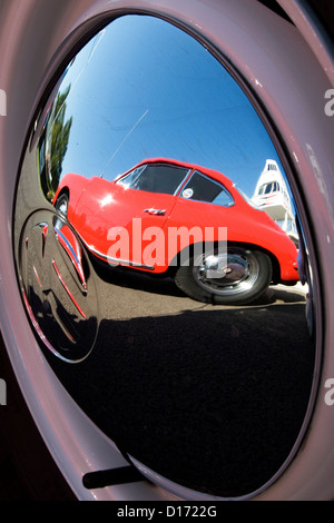 Die Reflexion eines roten Oldtimers in einem glänzenden Chrom-Radkappe. Stockfoto