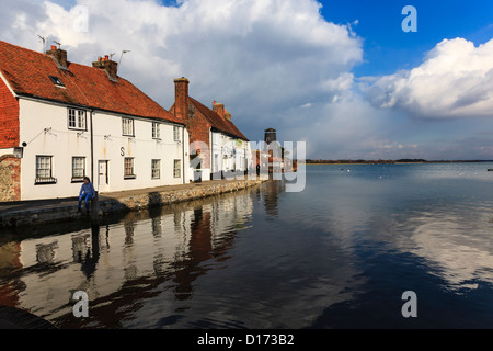 Ein junges Mädchen sitzt auf einem Tor und schwingt bei Flut, Langstone, mit dem Royal Oak Pub und Spiegelungen im Wasser, Hampshire Stockfoto