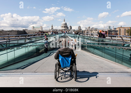 Obdachloser in Rollstuhl warten auf die Millennium Bridge mit Blick auf St. Pauls im Sonnenschein Stockfoto