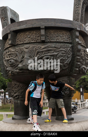 Kinder spielen, um eine riesige Messing Urne auf dem Tiger Hill in Suzhou, China. Stockfoto