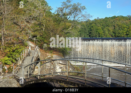 Geschwungene Fußgängerbrücke über Glane Fluss mit Wasserfall-Staudamm im Hintergrund, Saint-Junien, Limousin, Frankreich Stockfoto
