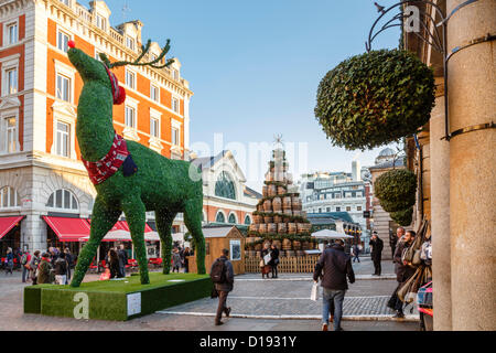 LONDON, 11. Dezember 2012, einem riesigen 32 ft hoch Formschnitt Rentier überragt Weihnachts-Einkäufer in Covent Garden in London. Ein Baum aus Jack Daniels Whisky Fässern steht im Hintergrund. Bildnachweis: Paul Maguire / Alamy Live News Stockfoto