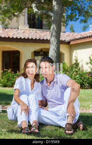 Ein junges attraktives Paar Mann und Frau Mann und seine Frau saß auf ihrem Rasen in den Sommer Sonnenschein glücklich lächelnd zusammen Stockfoto