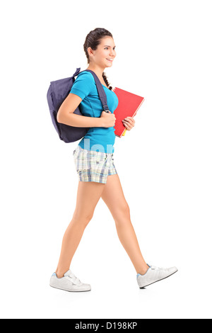 In voller Länge Portrait von einer Studentin mit Rucksack zu Fuß und hält Buch isoliert auf weißem Hintergrund Stockfoto