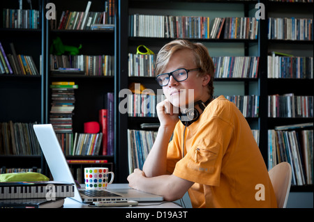 Confident entspannt Teenager Schuljunge mit Kopfhörern mit einem Laptop-Computer und Smartphone mit seine Musiksammlung in b/g Stockfoto