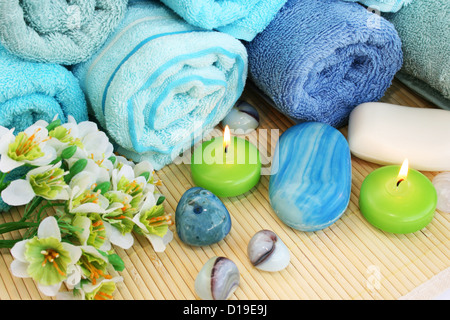 Stapel Handtücher, Kerzen, Steinen, Blumen auf Matten Hintergrund. Stockfoto