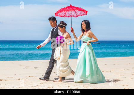 Hochzeitsfeier am Pansea Beach, Surin Beach, Phuket, Thailand - Braut, Bräutigam und Brautjungfer mit roten Sonnenschirm Stockfoto