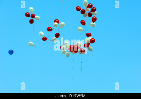 Rote und weiße Ballons mit einem blauen, der auf der Brise gegen einen blauen Himmel schwebt Stockfoto