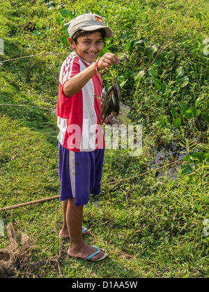 Ein Junge paraguayischen lächelt wie er blickt nach vorne hält seine frisch gefangenen Fisch aus einem Bach in der Nähe seiner Heimat. Stockfoto