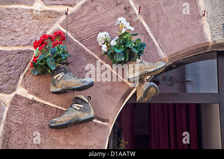 Alte Wanderschuhe, die über dem Eingang mit Blumen in ihnen hängen, entlang des Camino de Santiago de Compostela, Stockfoto