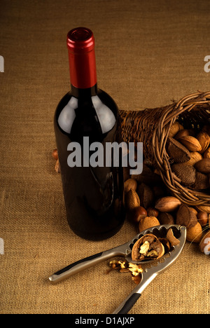 Sortiment von Nüssen in Korb mit Flasche Rotwein und Nussknacker auf braunem Hintergrund Stockfoto