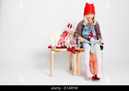 Studioportrait von fröhliches junges Mädchen auf Stuhl sitzen und spielen mit Spielzeug Weihnachten Elfen Puppen Stockfoto