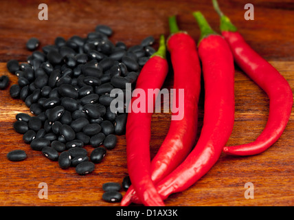 Rote Chilischoten und rohe schwarze Bohnen auf ein Schneidbrett aus Holz Stockfoto