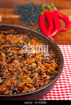 Scharf und würzig Chili Con Carne in der Pfanne mit Reis. Ganze Paprika und schwarzen Rohbohnen im Hintergrund. Stockfoto