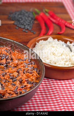 Scharf und würzig Chili Con Carne in der Pfanne mit Reis. Ganze Paprika und schwarzen Rohbohnen im Hintergrund. Stockfoto