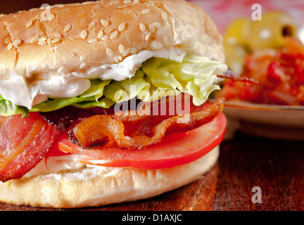 BLT Bacon, Salat, Tomate und Frischkäse Sandwich in einem Brötchen mit Oliven und Gurke im Hintergrund Stockfoto