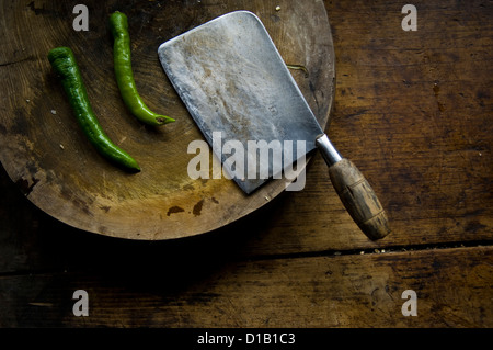 ein Messer und zwei grüne Chilischoten auf einer Holzplatte Stockfoto