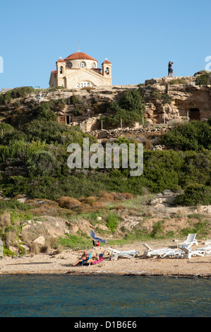 Urlauber-Sonnenbaden nördlich von Coral Bay Agios Georgios Pegeias übersehen durch eine Kirche mit dem gleichen Namen. Zypern Stockfoto